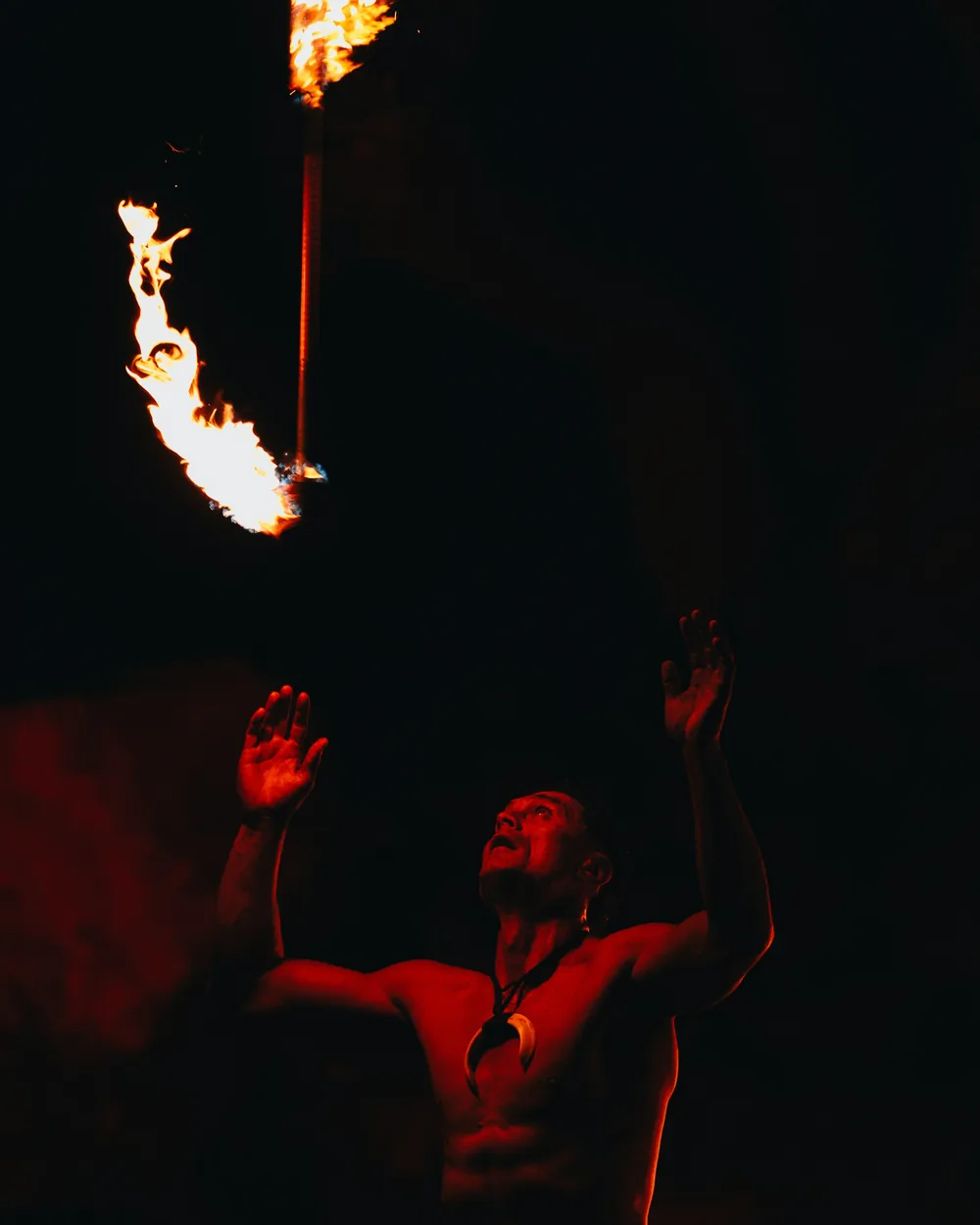 Polynéský umělec s ohněm a noži držící zapálenou pochodeň nad hlavou proti tmavé noční obloze (reprezentativní fotografie, nejde o Chief's Luau)
